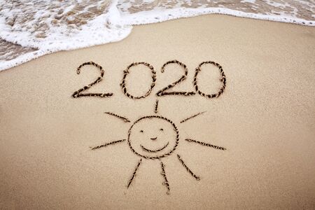 Year 2020 written at the caribbean sand beach with Sun drawingの写真素材