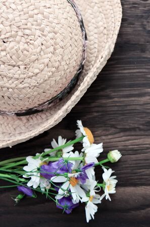 Summer flowers with a straw sun hat on brown wood background.の写真素材