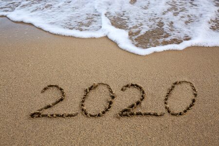 Year 2020 written at the caribbean sand beach with sea wave .