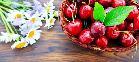 Cherries in the basket pot and daisies on an old wooden background.の写真素材