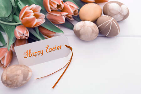 Easter card with bouquet of tulips and colorful eggs on white wooden .