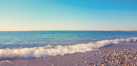 Summer panoramic view of the sea and sun on gravel beach.