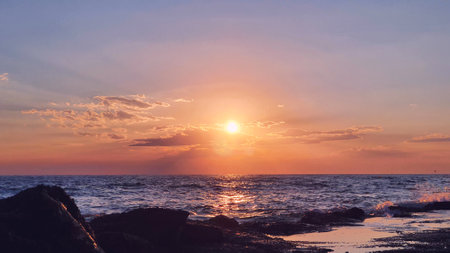 Colorful sunset with large sun under the sea waves.