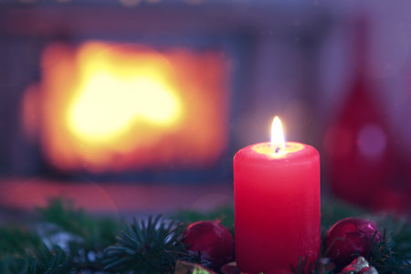 Burning red Advent candle in a warm interior with fireplace.の写真素材