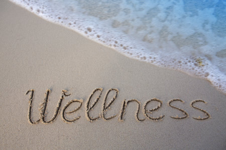 Word wellness written on the sand of the beach. Beach and waves background.