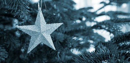 Close up of silver Christmas star on fir tree. Bokeh garlands in the background.