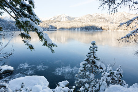 Mountain reflection in lake in winter with snow covered trees and blue sky