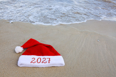 New Year 2027 written at the Santa Claus hat on caribbean beach.