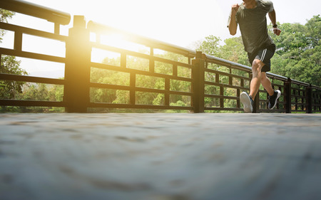 Attractive fit man running fast along bridge at a park, black man doing workout outdoorsの写真素材