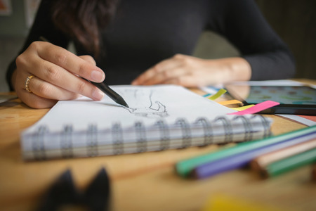 Close-up of young creative fashion designer working hard on project at a modern home officeの写真素材