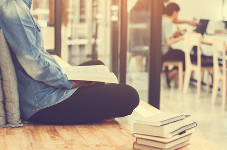 Beautiful student woman sitting at the stair and reading a book with blurred cafe workplaceの写真素材