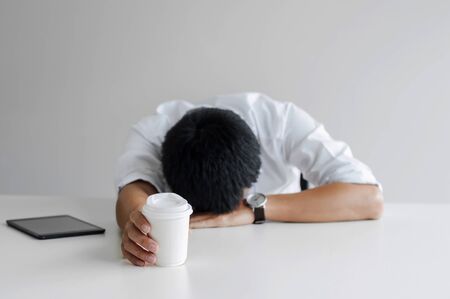 Tired business man take a nap with coffee at a workplaceの写真素材