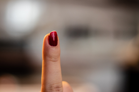 a closeup shoot to woman finger with red nail polish, background is blurry. finger pointing up.
