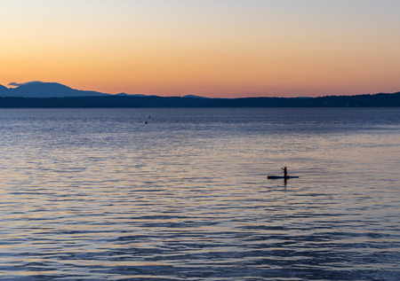 A woman kneels on her paddleboard during the sunset on Puget Sound near Seattle