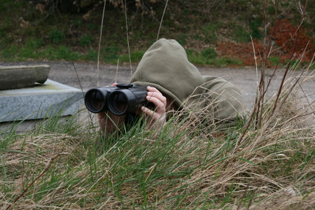 A man with binoculars sits on a grass in the park and is observing.の写真素材