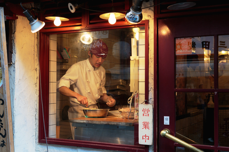 TOKYO - JAPAN - DECEMBER 26, 2015: A Chef prepares food behind a restaurant window in Shinjuku area, downtown Tokyo.のeditorial素材