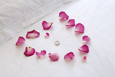 A pink heart made of rose petals on a crisp white bed enclose a diamond engagment ringの写真素材