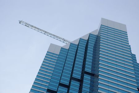 A skyscraper building with blue tinted glass in the foreground a  crane in the background