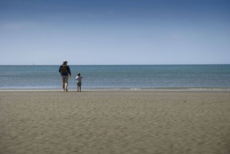 A father and son take a walk to explore the waves breaking on the shore of the beach in Stanley, Hong Kongの写真素材