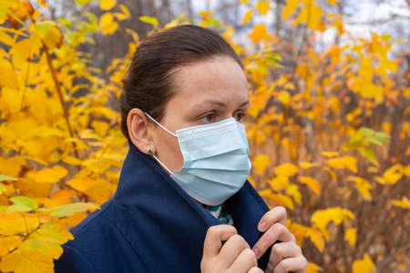 Woman with a medical face mask at outdoor in autumn park.の写真素材