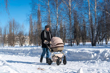 Tired father walking with baby carriage in winter parkの写真素材