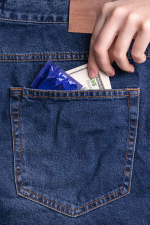 A woman's hand pulls money out of the back pocket of her jeans. Dollars and a condom in your pocketの写真素材