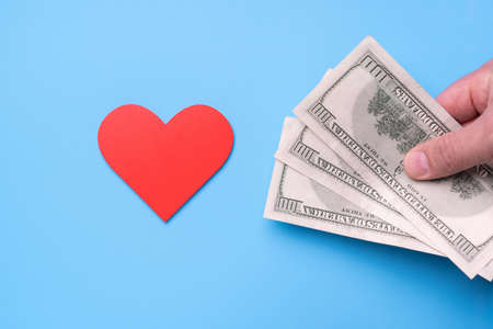 Man's hand with dollars stretches out his hand to a red heart on a blue background, Donateの写真素材