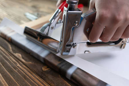 The process of stretching a synthetic canvas with a printed photo onto a wooden stretcher. Hand with stapler and forcepsの写真素材