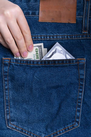 Woman's hand puts a 100 dollar bill and a condom in the back pocket of jeansの写真素材