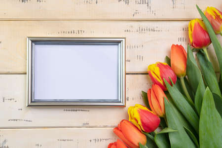 Bouquet of red tulips on a beige wooden background and a silver frame for text, copy-spaceの写真素材