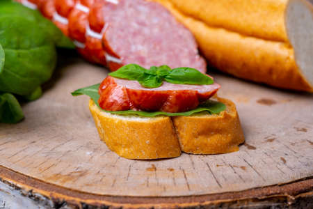 A simple sausage sandwich. A slice of cervelat, spinach and basil sprigs lie on a baguetteの写真素材