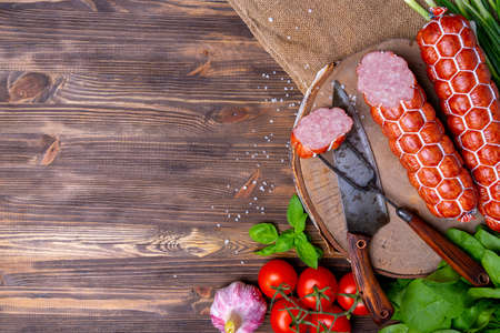 Homemade sausage with vegetables on a wooden background, top view. Knife and fork with a slice of sausageの写真素材