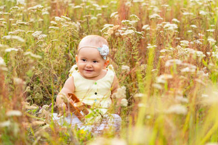 Toddler sits in the grass on a field among wildflowers with a wooden toy airplane in his handsの写真素材