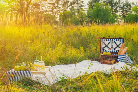 Summer picnic at sunset. A beautiful equipped picnic area with all the accessories. A wicker picnic box, a white blanket and various fruits. Sunlightの写真素材