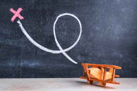 A wooden biplane toy on the background of a blackboard with a loop and a cross drawn in chalk. The concept of recreation and choosing a country for a vacationの写真素材