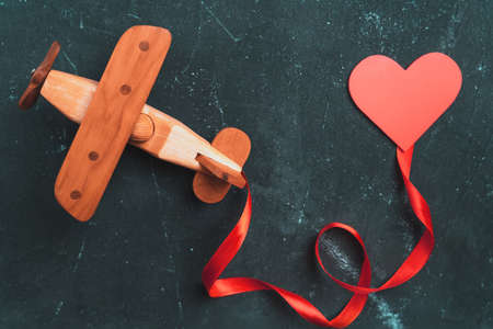 Wooden toy airplane biplane on a dark background with a red ribbon and a heart.の写真素材