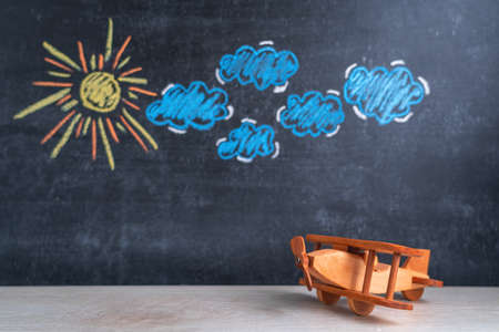 Wooden toy airplane biplane on the background of a chalk board with a pattern of clouds and the sun