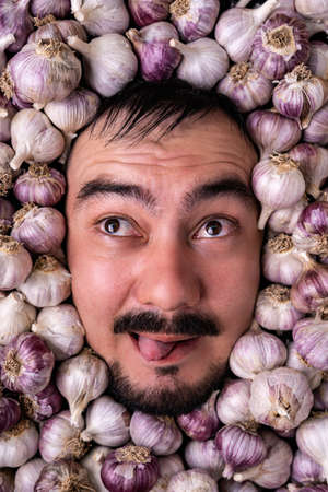 Portrait of a bearded man showing his tongue among garlic bulbsの写真素材