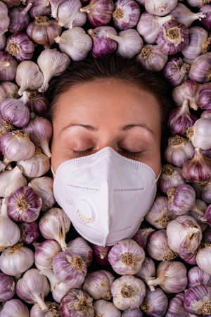 A girl with closed eyes in a medical mask among a lot of garlic bulbsの写真素材