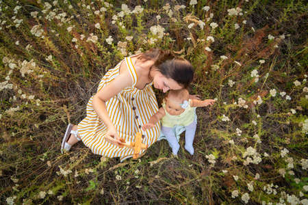 Mom and newborn baby play with a wooden toy biplane among the wildflowers. Portrait of a happy mother and newborn daughter in a field in the countryside.Top viewの写真素材