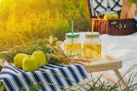 Summer picnic at sunset. A beautiful equipped picnic area with all the accessories. A wicker picnic box, a white blanket and various fruitsの写真素材
