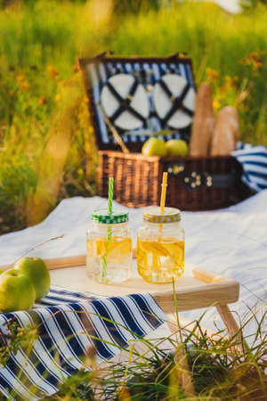 A picnic spot. Cans of lemonade stand on a small stand and a wicker box with picnic dishes in the backgroundの写真素材