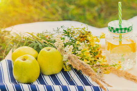 Cans of lemonade on the picnic table. Wildflowers and green apples are nearby. Close upの写真素材