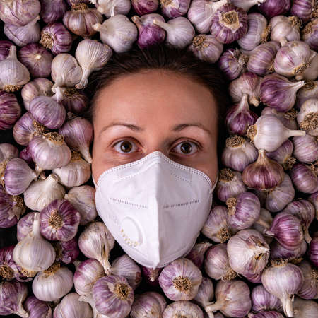 A girl in a medical mask among many garlic bulbs, square framingの写真素材