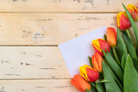 Bouquet of red tulips on a beige wooden background white sheet of paper for text, copy-spaceの写真素材