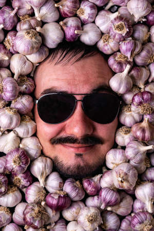 Portrait of a smiling brutal bearded man in black sunglasses among garlic bulbsの写真素材