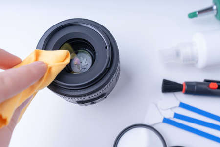 The photographer's hand with yellow microfiber wipes the camera lens. White backgroundの写真素材