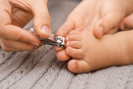 Mom gently cuts the toenails of the baby sleeping on a gray blanket, selective focusの写真素材