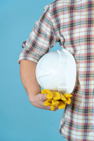A worker in a plaid shirt with a protective helmet and gloves on a blue background.の写真素材