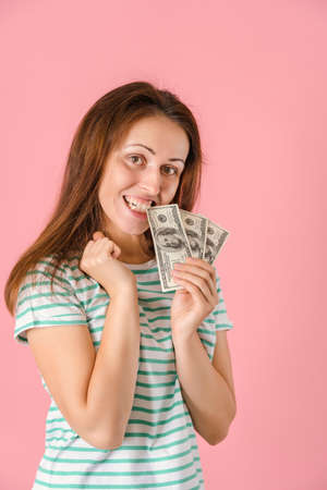 A joyful middle-aged girl smiles holding a fan of hundred-dollar bills in her hands while standing on a pink background. Vertical photoの写真素材